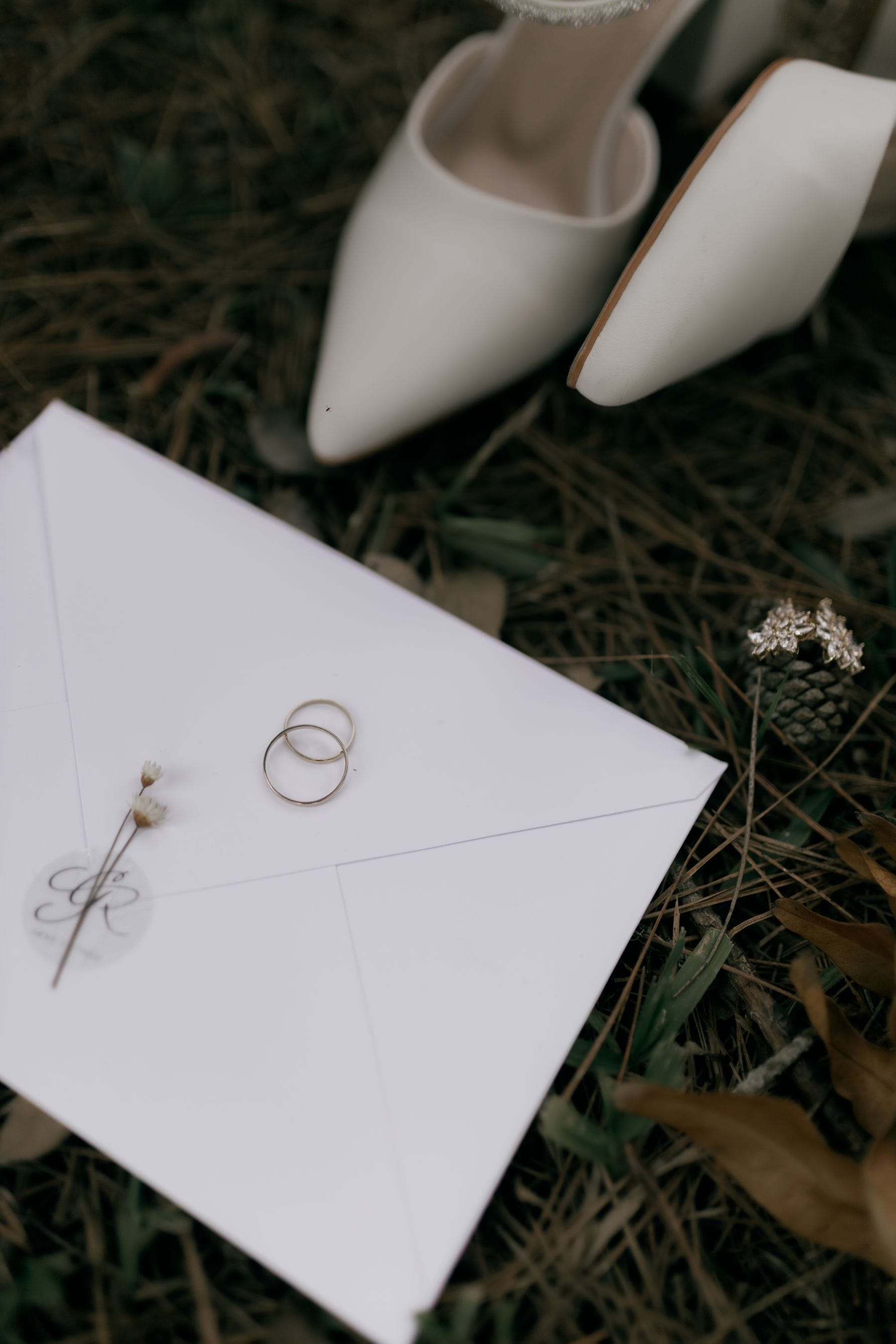 Wedding invitation, rings and shoes laid out on grass