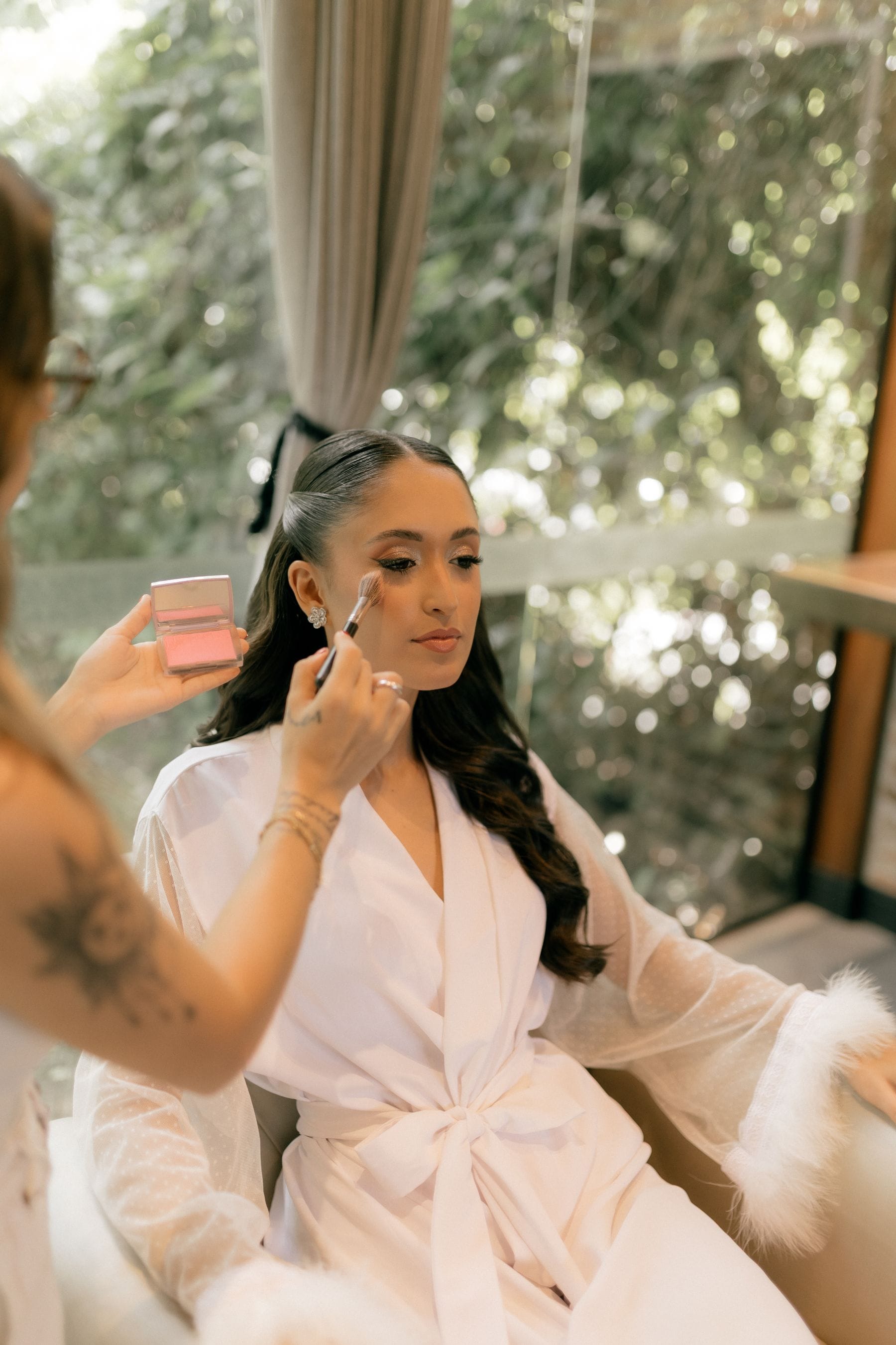 Makeup being done by a window on the wedding morning